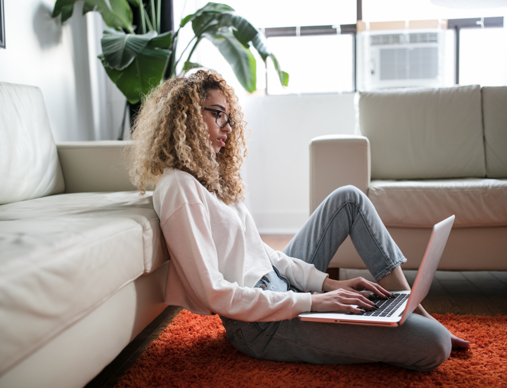 African American woman writing on laptop sitting on the floor